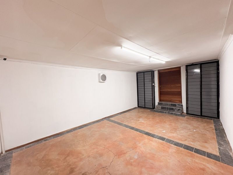 A spacious, empty garage featuring concrete flooring with decorative tile inlays, secure metal gates, and a timber entrance door.