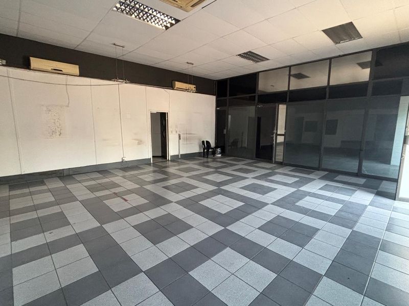 Spacious open-plan retail or office area featuring tiled flooring, suspended ceilings, and large glass partitions, offering a versatile layout for various business needs.