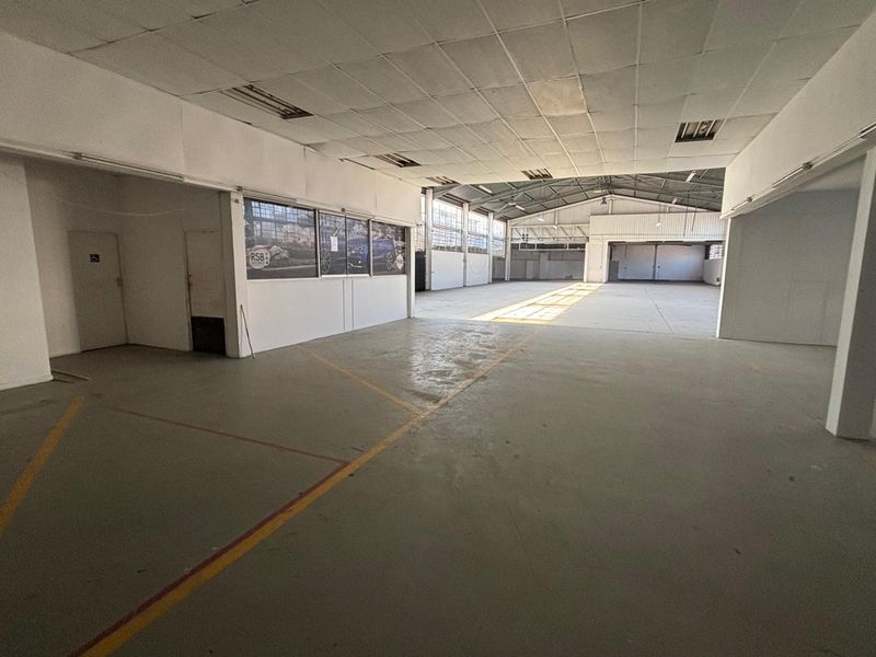 Spacious open-plan retail or industrial warehouse area featuring high ceilings, concrete flooring, and large windows providing ample natural light.