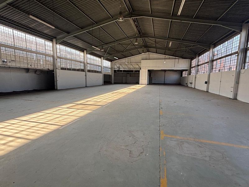 Spacious industrial warehouse unit featuring high ceilings, steel truss roofing, large windows for natural light, and durable concrete flooring.
