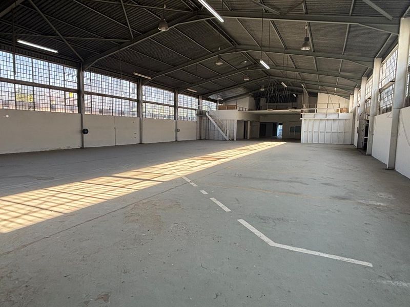 Spacious industrial warehouse featuring high ceilings, large steel-framed windows for natural light, concrete flooring, and a mezzanine level suitable for various commercial uses.