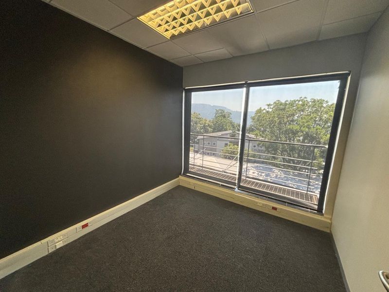 An empty office space featuring a dark accent wall, carpeted flooring, recessed ceiling lighting, and a sliding glass door leading to a balcony.