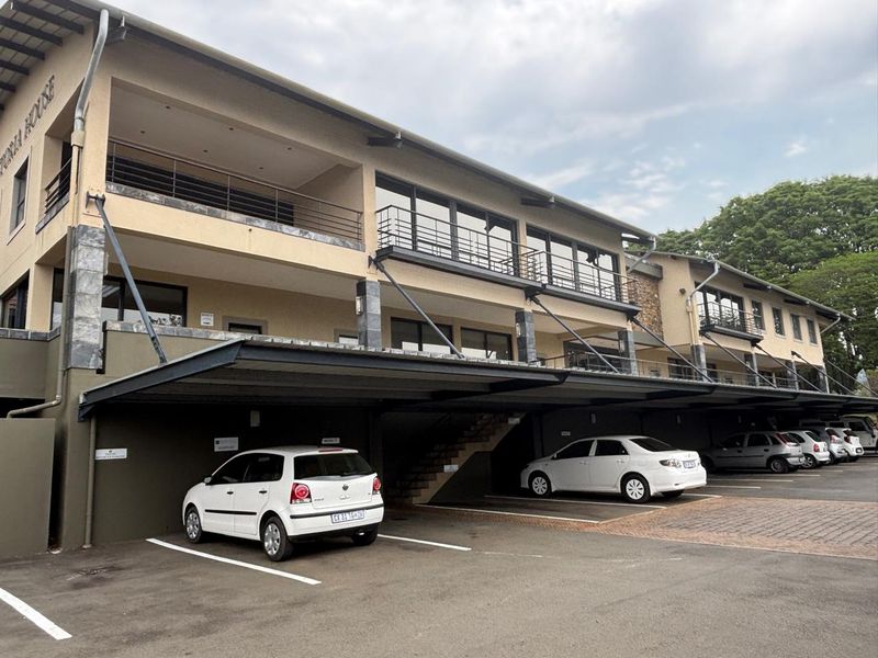 A multi-story office building featuring covered parking bays, private balconies with metal railings, and stone-clad architectural accents.