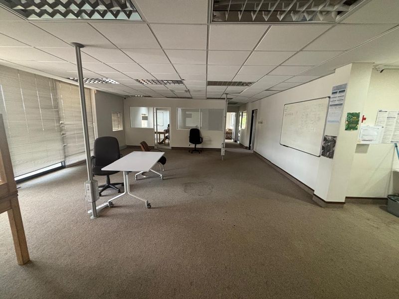 Open-plan office space featuring suspended ceilings, recessed lighting, carpeted flooring, and a partitioned glass office area, suitable for a professional workspace.