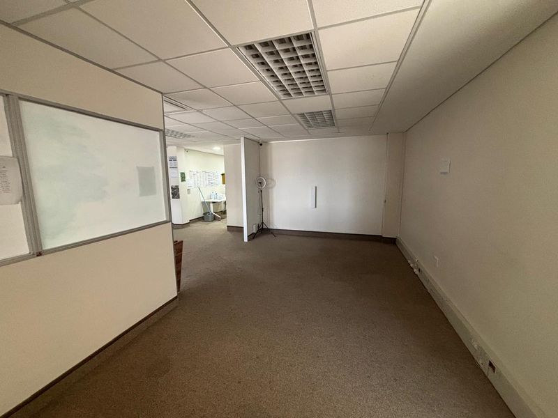 A vacant office space featuring a suspended ceiling with recessed lighting, carpeted flooring, and a built-in whiteboard partition.
