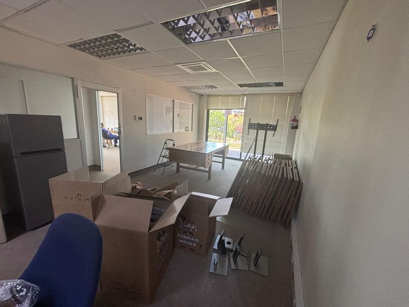An office space featuring a suspended ceiling with recessed lighting, glass partitioning, and window blinds, currently in need of maintenance and clearing.