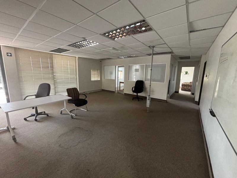 Spacious office area featuring suspended ceilings, recessed lighting, carpeted flooring, and glass partition walls, offering a functional workspace layout.