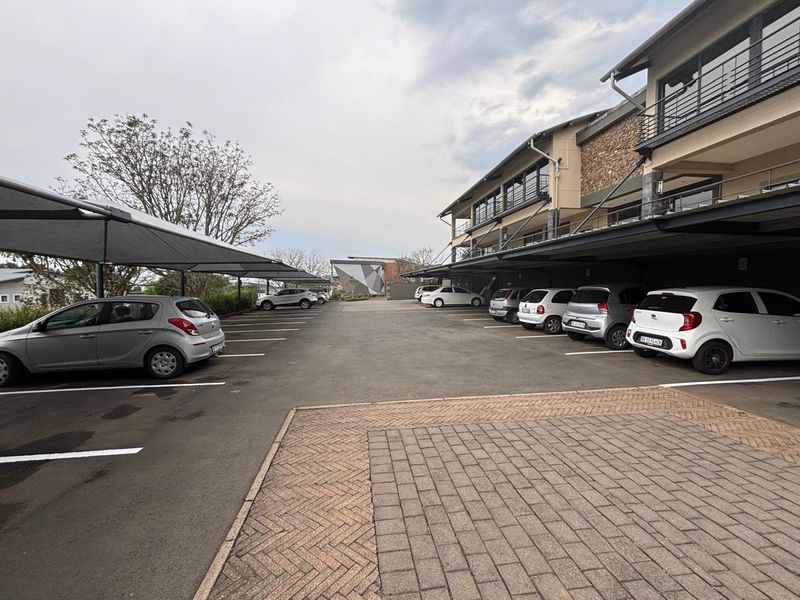 Exterior view of an office property featuring a paved parking area with covered shade cloth carports and a multi-story building facade.