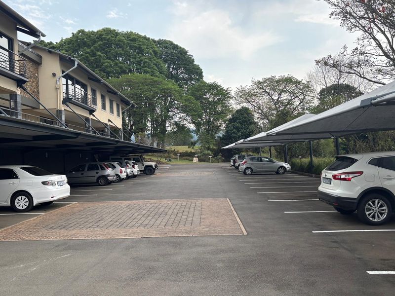 Exterior view of an office property featuring a paved parking lot with covered carports and a multi-story building with balconies.