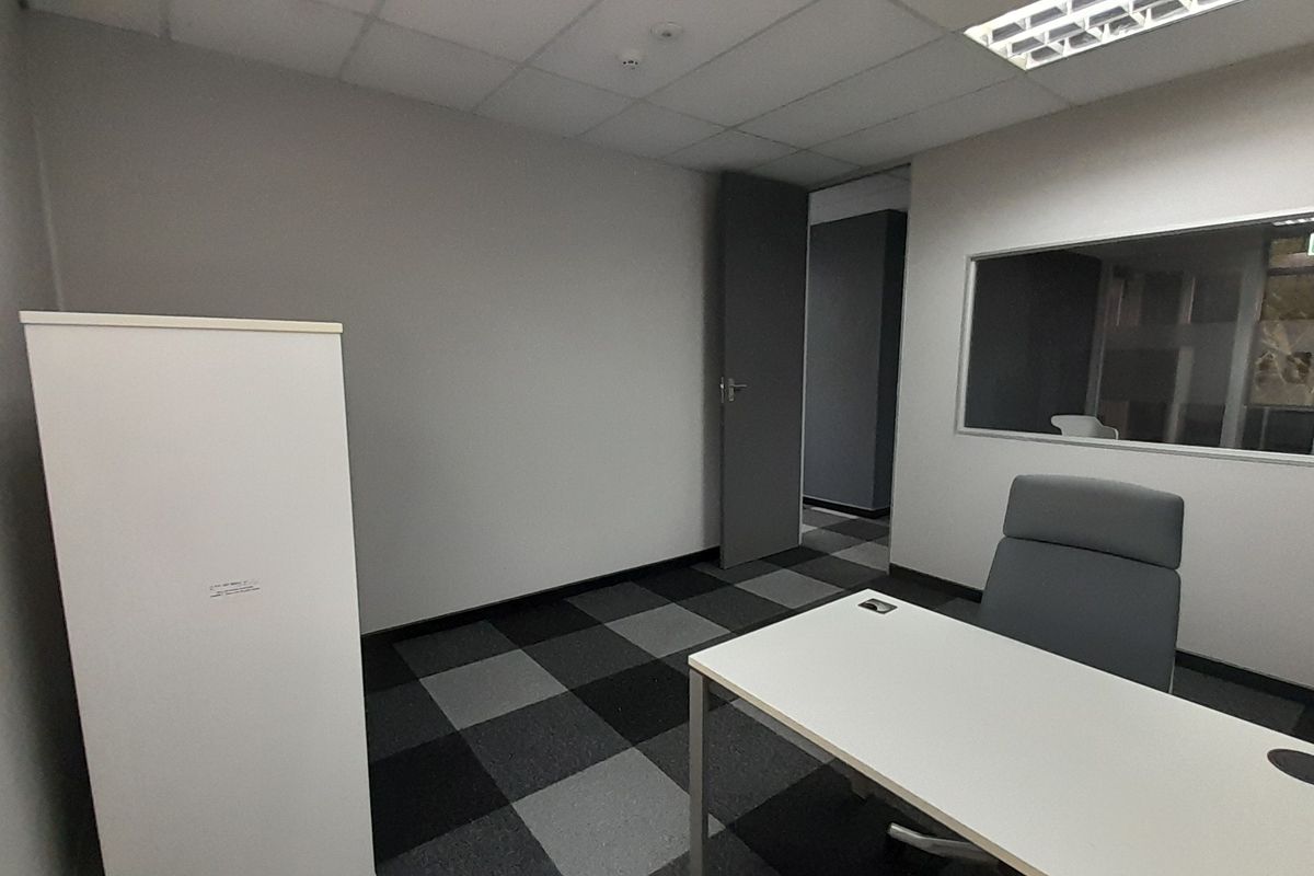 A functional office space featuring carpet tiles, a suspended ceiling with recessed lighting, and an internal glass partition for natural light.