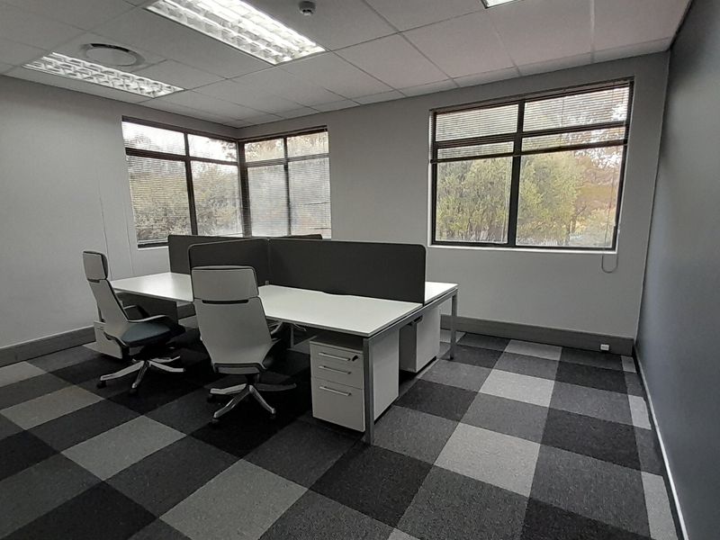 A professional office space featuring carpeted flooring, suspended ceilings with recessed lighting, and large windows providing natural light.