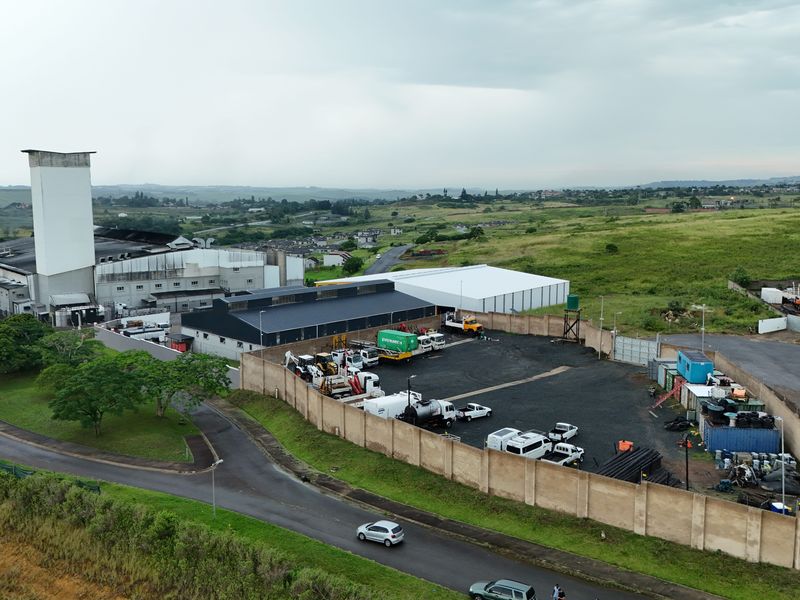 Aerial view of an industrial facility featuring a large warehouse, processing tower, and a secure, fenced yard area with ample space for logistics.
