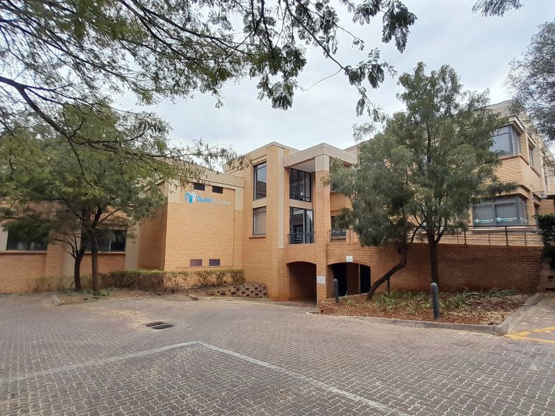 Front exterior view of a multi-level brick office building featuring a paved driveway, covered parking access, and established garden landscaping.