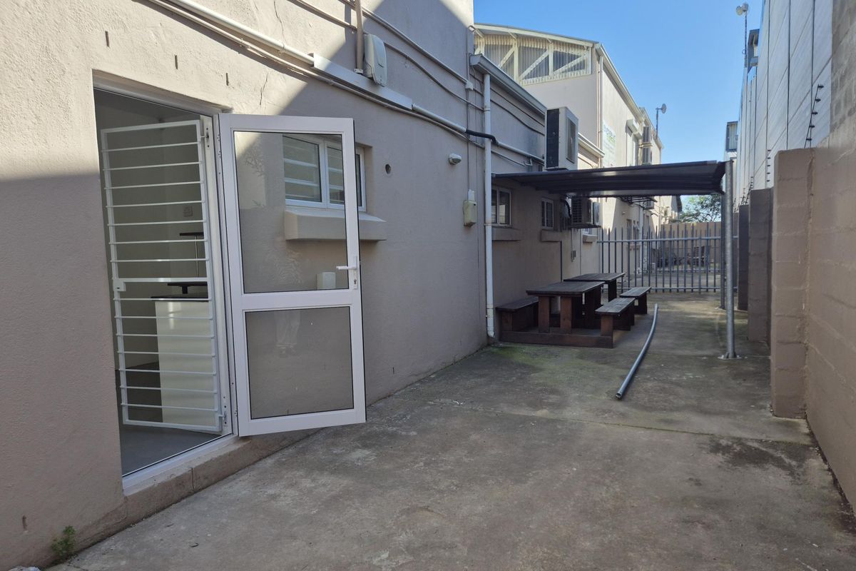 Rear exterior area featuring a concrete courtyard, covered seating space, and direct access to the building interior via a security door.