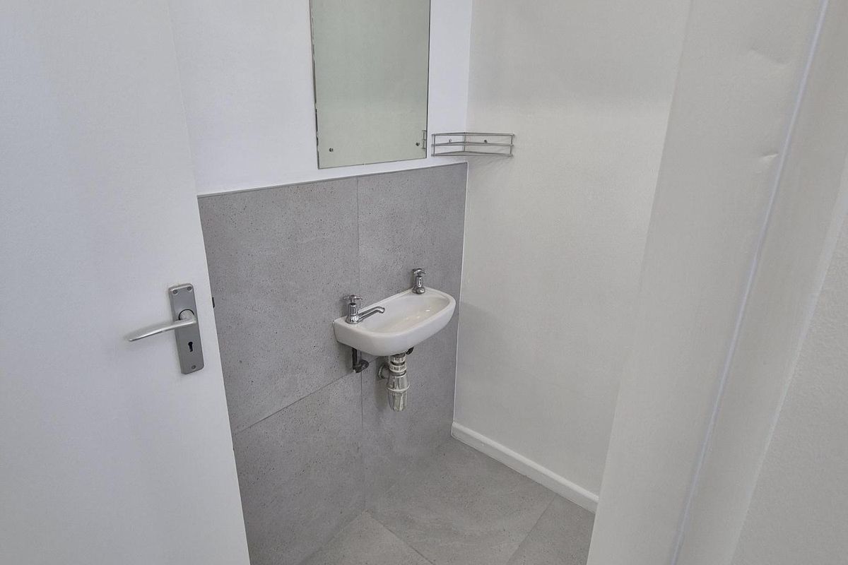 A compact guest bathroom featuring a wall-mounted basin, grey tiled splashback, and floor tiling.