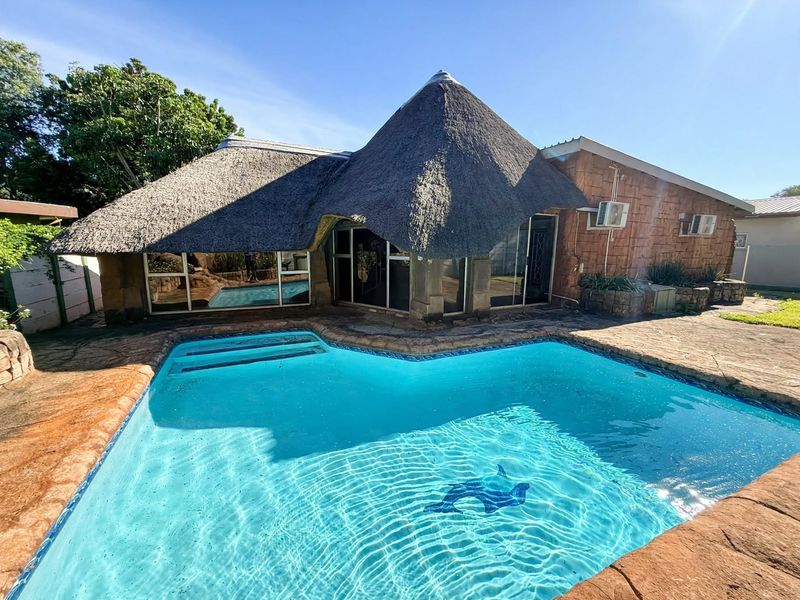 Outdoor pool area featuring a swimming pool with stone paving and a distinctive thatch-roofed building structure.