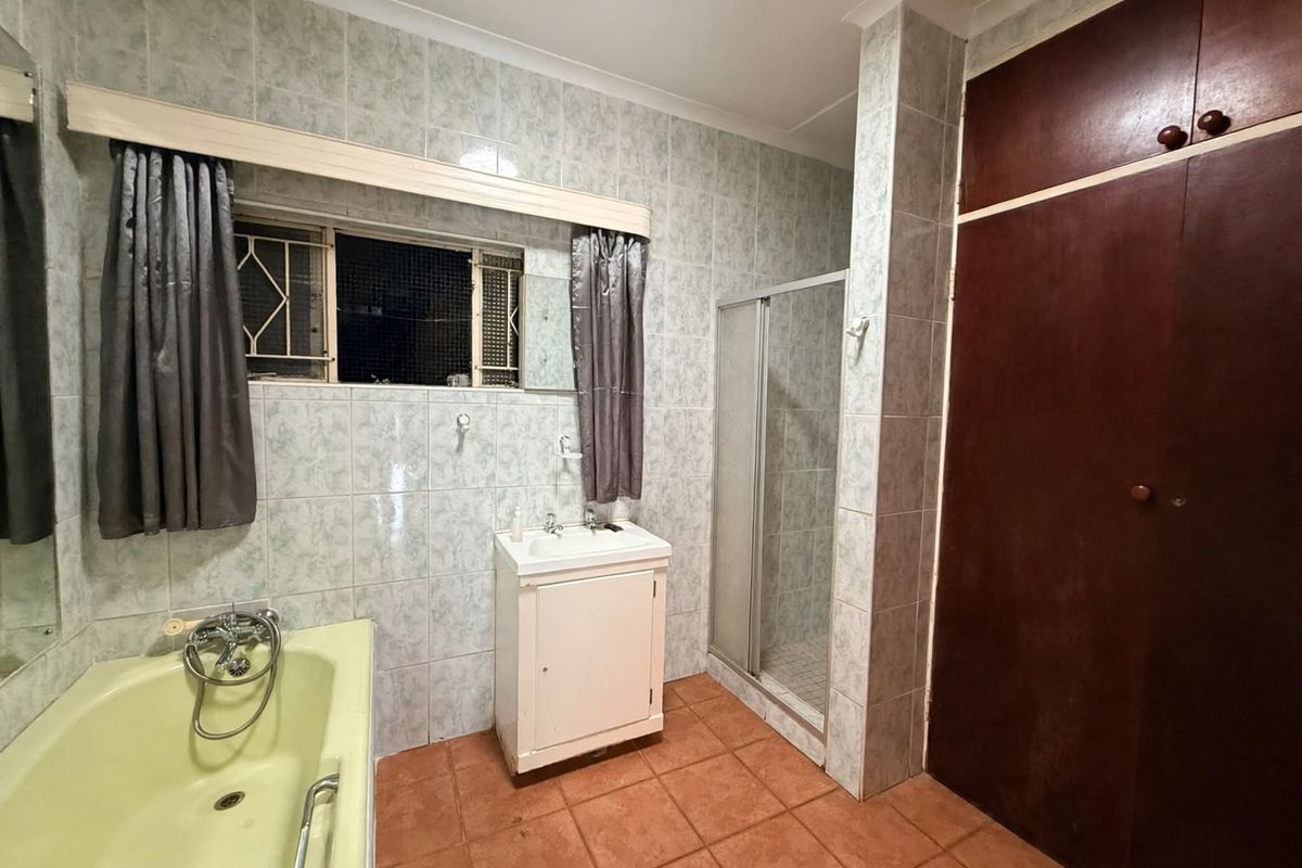 A dated bathroom featuring a bathtub, separate shower enclosure, vanity unit, and built-in storage cupboard with tiled finishes throughout.
