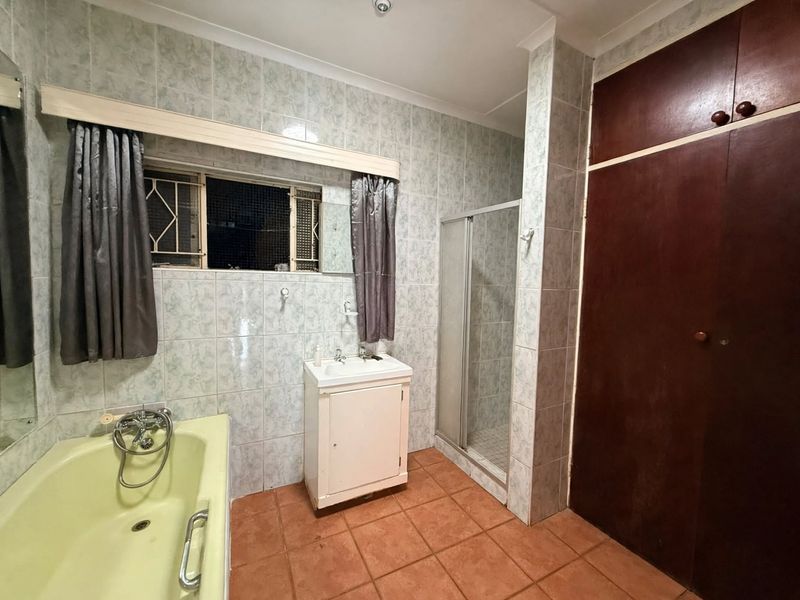 A dated bathroom featuring a bathtub, separate shower enclosure, vanity unit, and built-in storage cupboard with tiled finishes throughout.