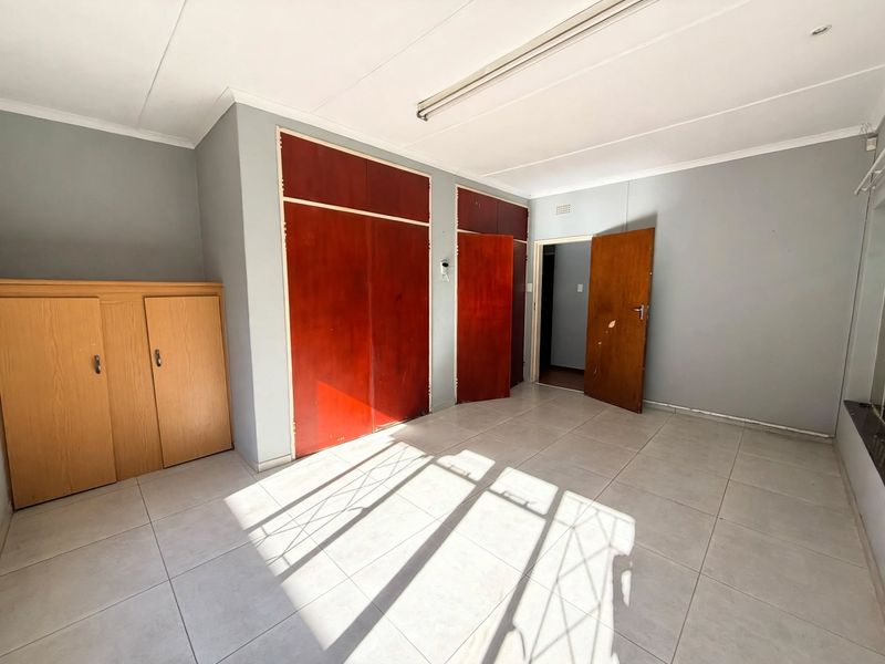 An empty office space featuring tiled flooring, built-in wooden cupboards, and a standard wooden door, offering a functional layout for a workspace.