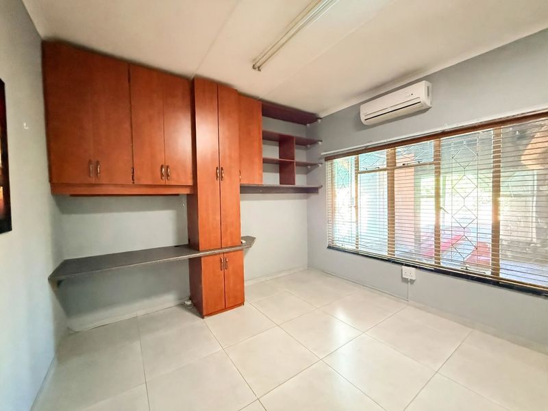 A functional office space featuring built-in wooden cabinetry, a desk area, tiled flooring, and an air conditioning unit, offering a clean and professional workspace.