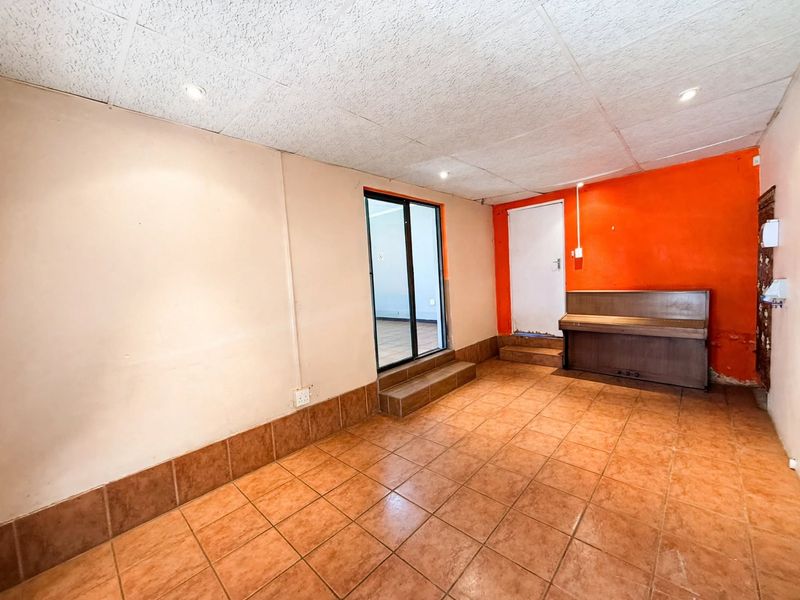 An empty office space featuring tiled flooring, recessed lighting, and a sliding glass door, with a distinct orange accent wall requiring cosmetic attention.