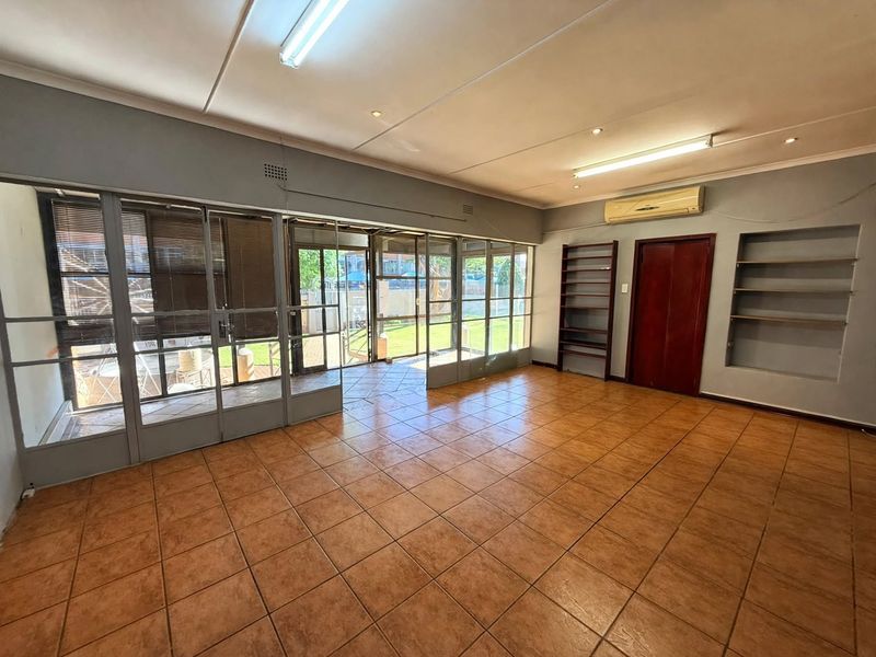 Spacious office area featuring tiled flooring, built-in shelving, air conditioning, and large glass doors providing natural light and access to the exterior.