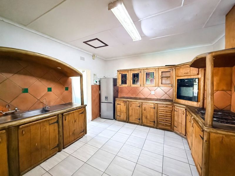 A functional kitchen featuring extensive built-in wooden cabinetry, tiled backsplash, integrated oven and hob, and a stainless steel sink with tiled flooring.