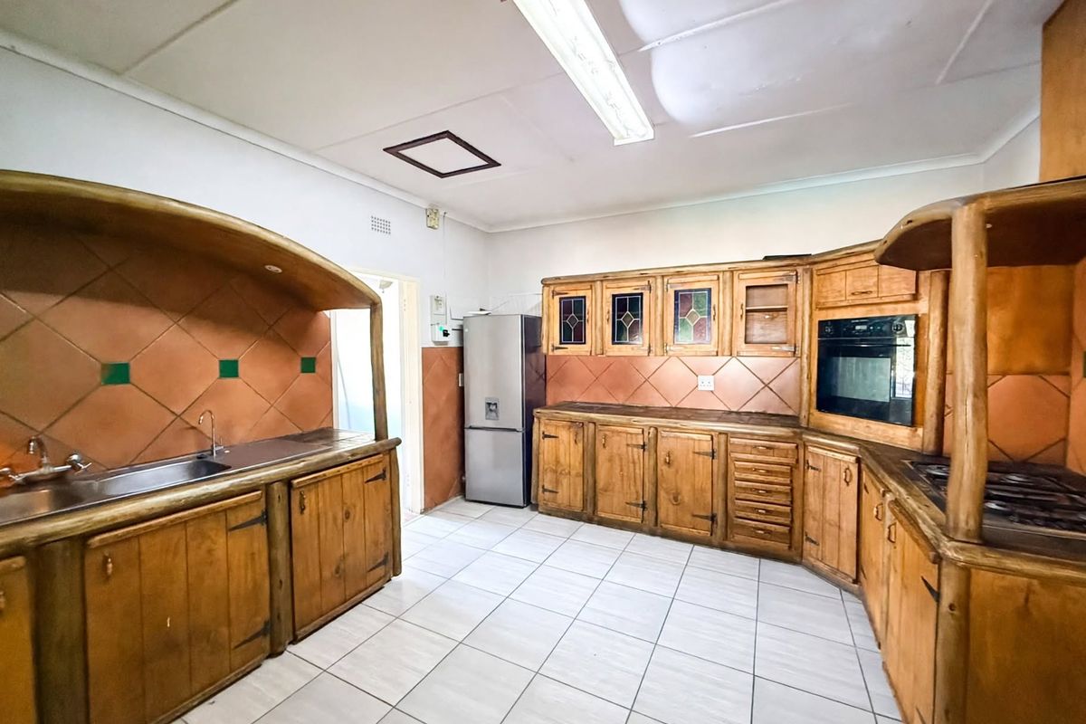 A functional kitchen featuring extensive built-in wooden cabinetry, tiled backsplash, integrated oven and hob, and a stainless steel sink with tiled flooring.