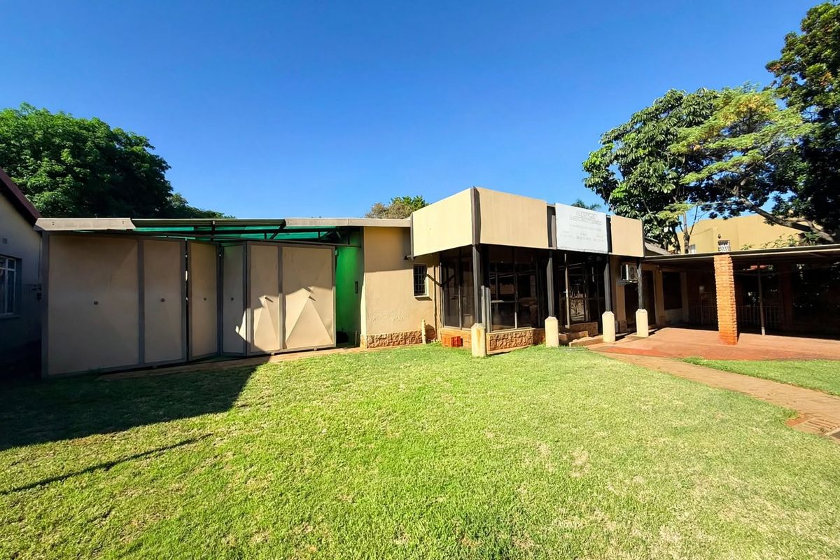 Rear view of the office property featuring a well-maintained lawn, paved walkway, covered patio area with brick pillars, and large glass windows.