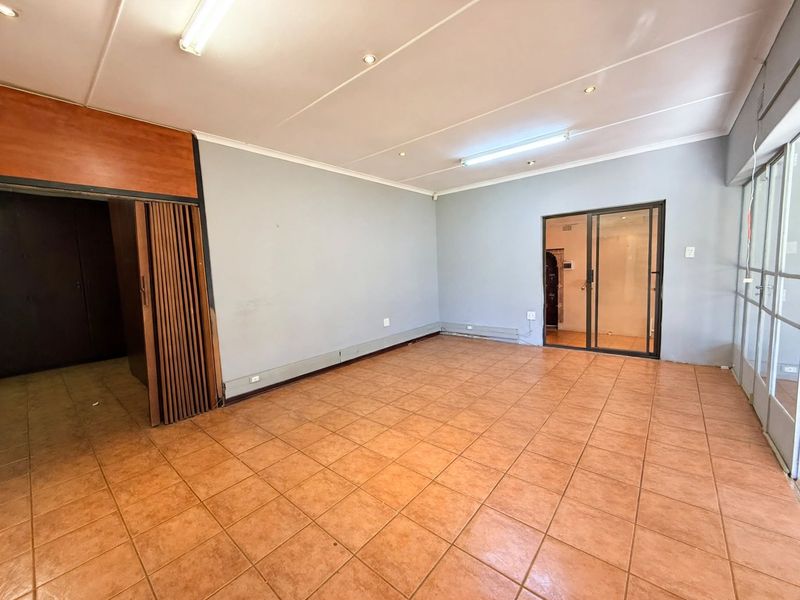 An empty office space featuring ceramic tile flooring, fluorescent lighting, and a functional folding room divider, offering a versatile layout for professional use.