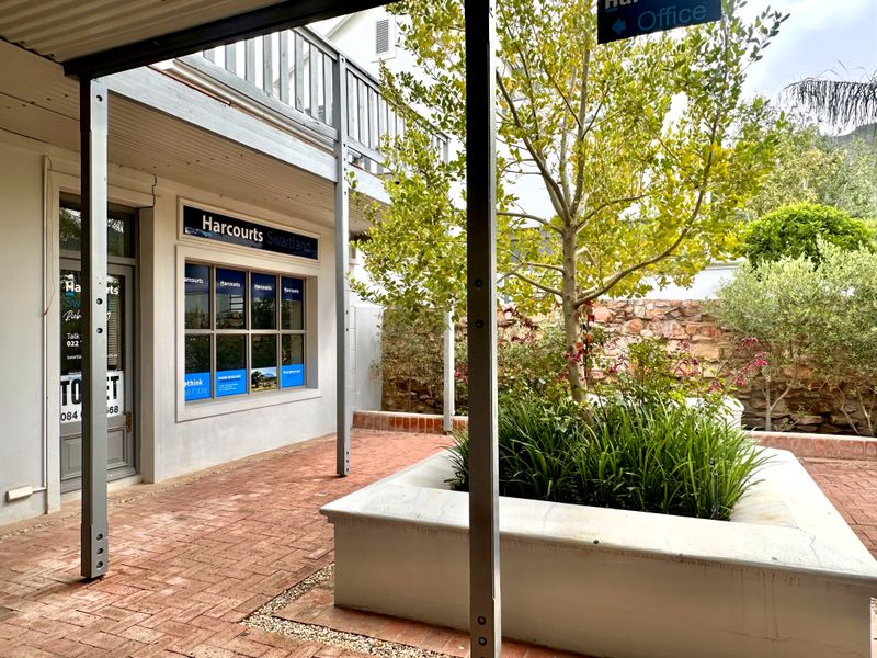 A well-maintained outdoor courtyard area featuring brick paving, a stone retaining wall, and a raised planter box, providing access to office premises.