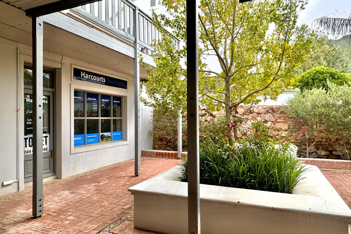 A well-maintained outdoor courtyard area featuring brick paving, a stone retaining wall, and a raised planter box, providing access to office premises.
