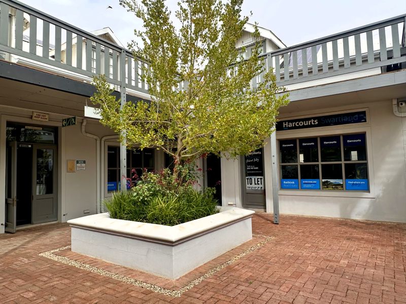A well-maintained commercial courtyard featuring brick paving, a central raised planter box, and office storefronts with balcony access above.