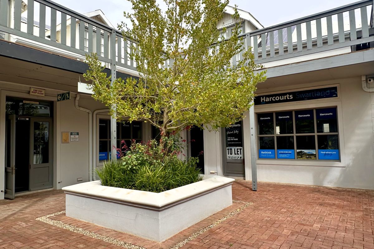 A well-maintained commercial courtyard featuring brick paving, a central raised planter box, and office storefronts with balcony access above.