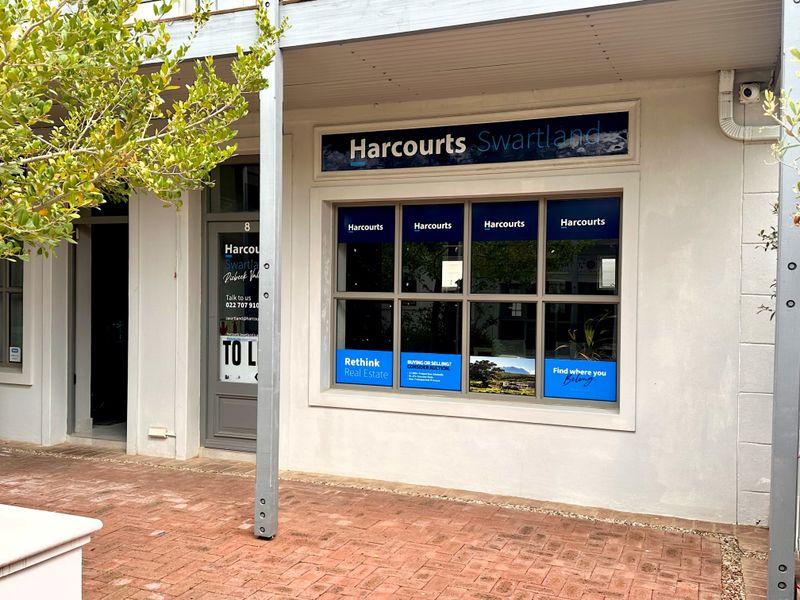 Front facade of a commercial office space featuring large display windows, covered walkway, and brick paved entrance area.