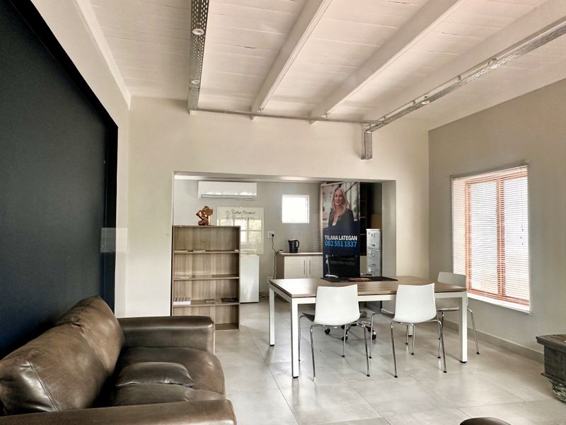 Modern office space featuring exposed ceiling beams, industrial-style electrical conduit, tiled flooring, and a split-system air conditioner.