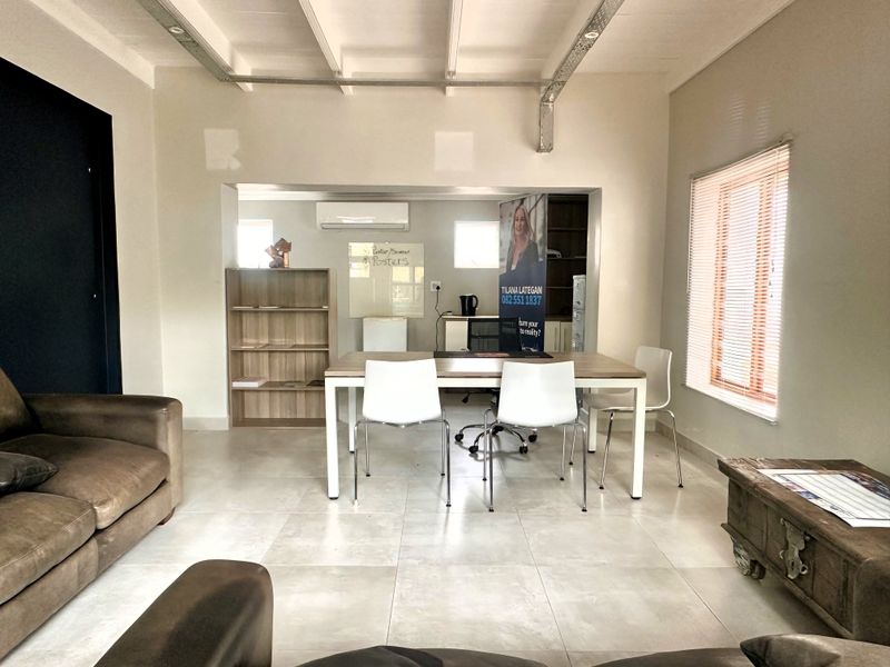 An open-plan office space featuring tiled flooring, exposed ceiling beams, and a wall-mounted air conditioning unit, offering a functional workspace environment.