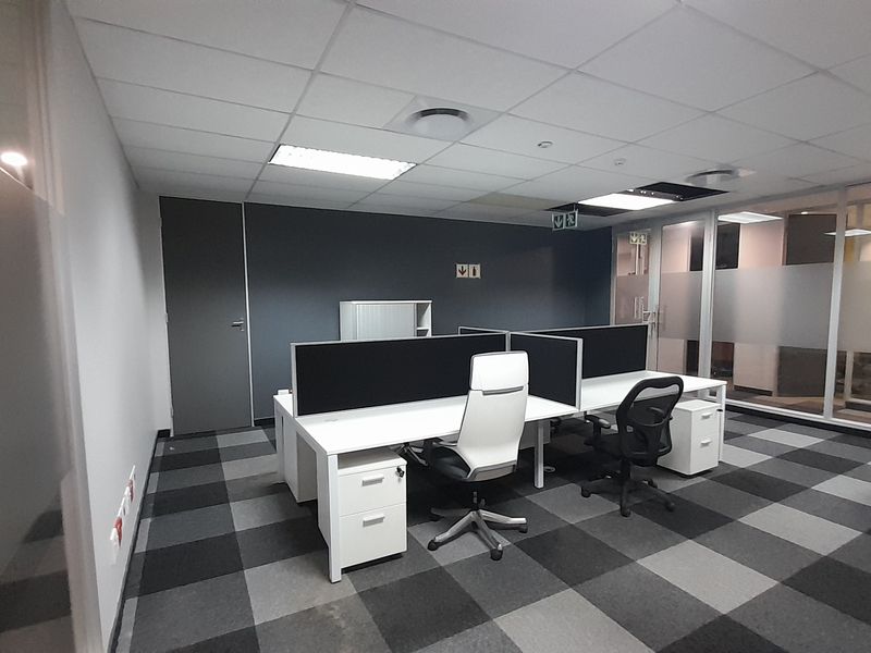 A modern office space featuring glass partitions, suspended ceilings with recessed lighting, and a professional checkerboard carpet tile finish.