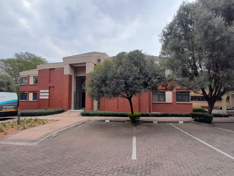 Front exterior view of a professional office building featuring a red brick facade, paved parking area, and established landscaping.