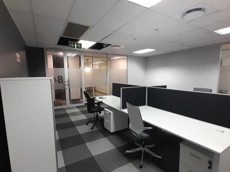A functional office space featuring glass partitions, carpeted flooring, and built-in desk workstations with integrated privacy screens.