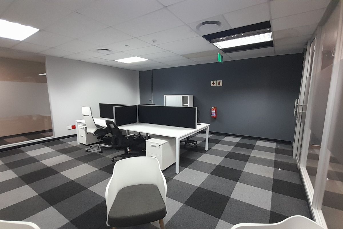 A modern office space featuring carpeted flooring, suspended ceilings with recessed lighting, and glass partitioning, providing a professional and functional work environment.