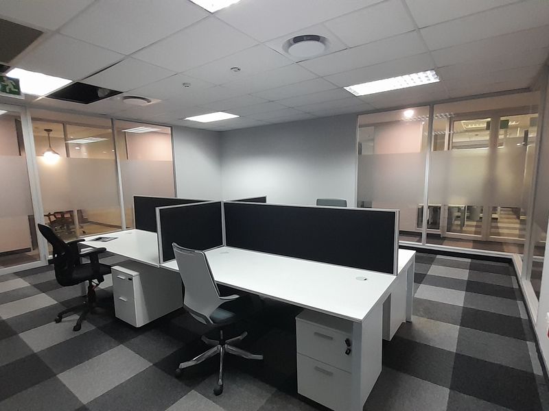 A modern office space featuring glass partitioning, suspended ceilings with recessed lighting, and professional carpet tiles, providing a clean and functional work environment.