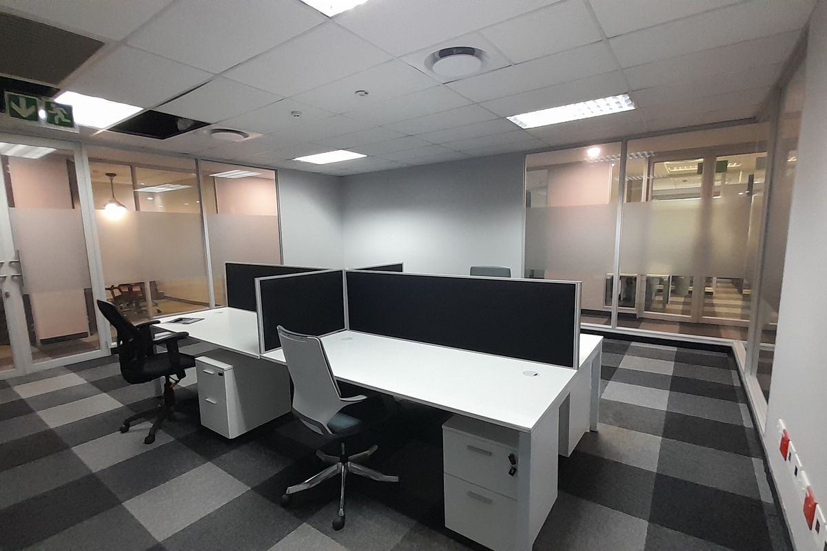 A modern office space featuring glass partitioning, suspended ceilings with recessed lighting, and professional carpet tiles, providing a clean and functional work environment.