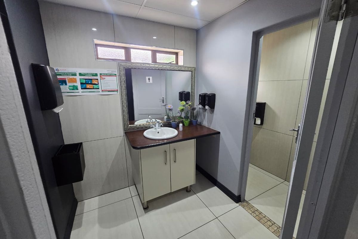 A clean commercial restroom featuring a vanity with a built-in basin, tiled flooring, and a separate toilet cubicle.