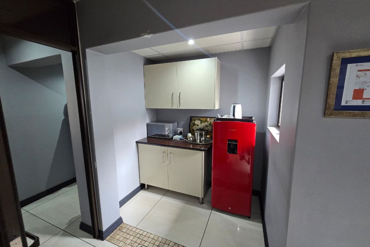 A compact kitchenette area featuring built-in cabinetry, tiled flooring, and a recessed layout suitable for office or utility use.