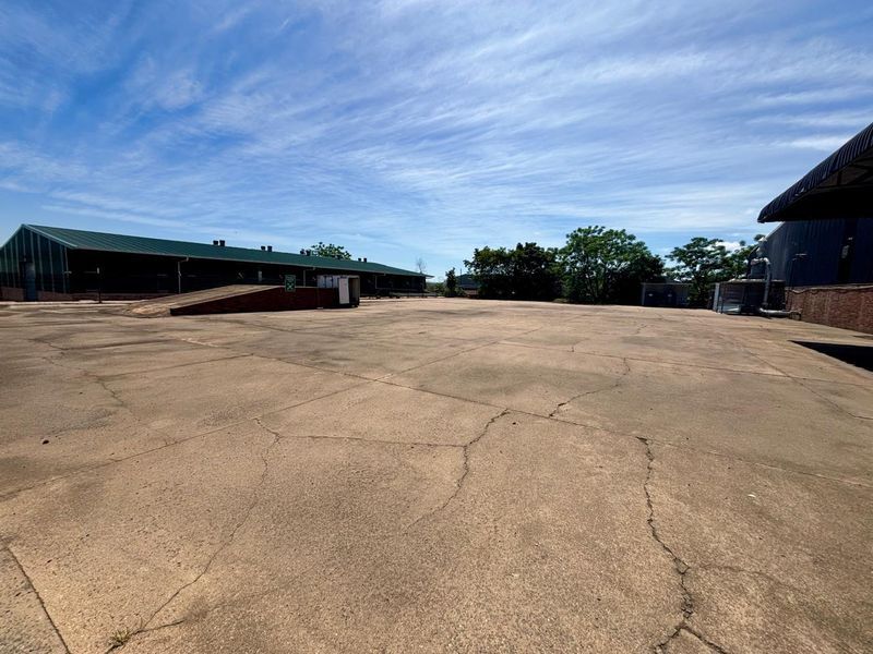 Expansive industrial concrete yard featuring a loading ramp and adjacent warehouse structures with metal roofing.