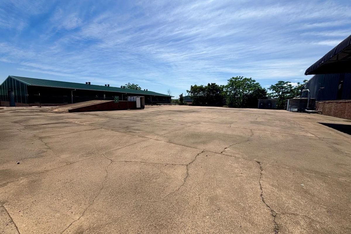 Expansive industrial concrete yard featuring a loading ramp and adjacent warehouse structures with metal roofing.