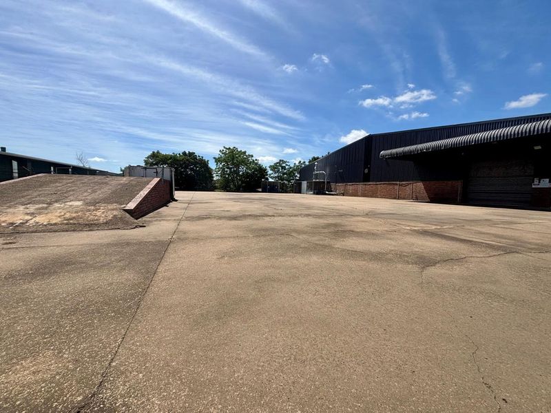Expansive commercial yard featuring a concrete loading ramp, asphalt surfacing, and access to a large industrial warehouse building with metal cladding.