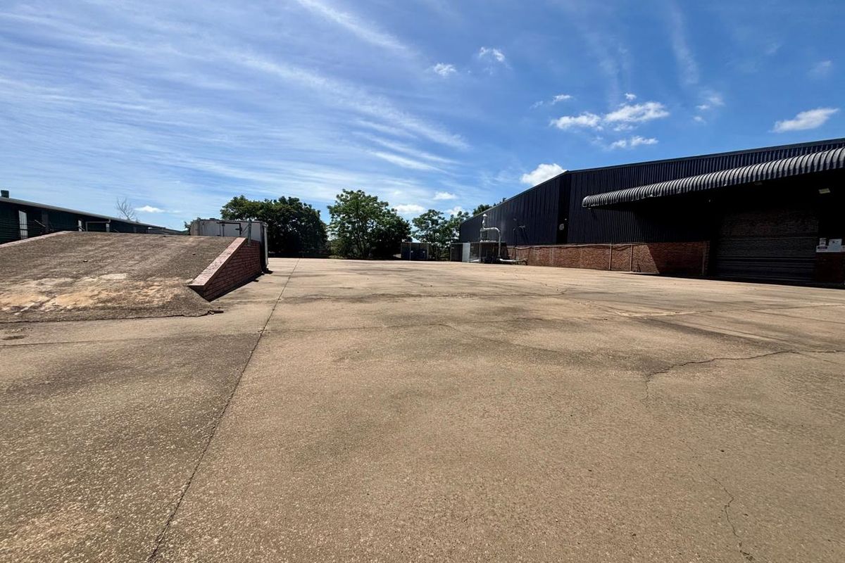 Expansive commercial yard featuring a concrete loading ramp, asphalt surfacing, and access to a large industrial warehouse building with metal cladding.