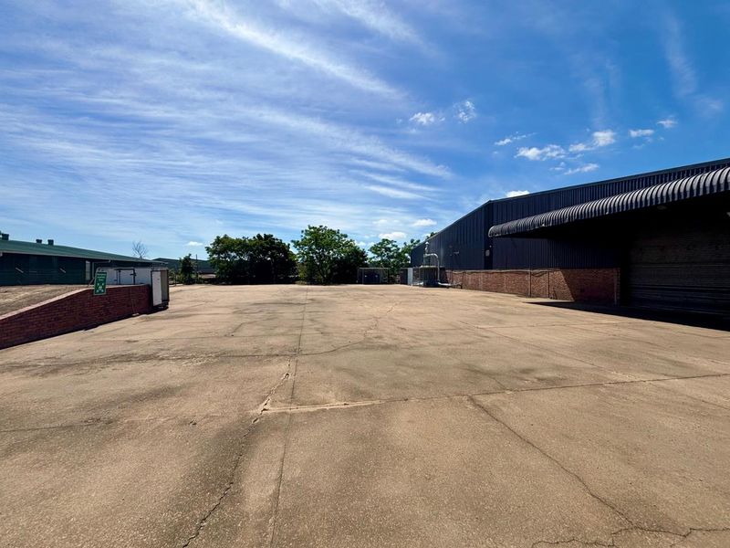 A spacious commercial concrete yard featuring a large warehouse building with a covered loading bay and brick retaining wall.